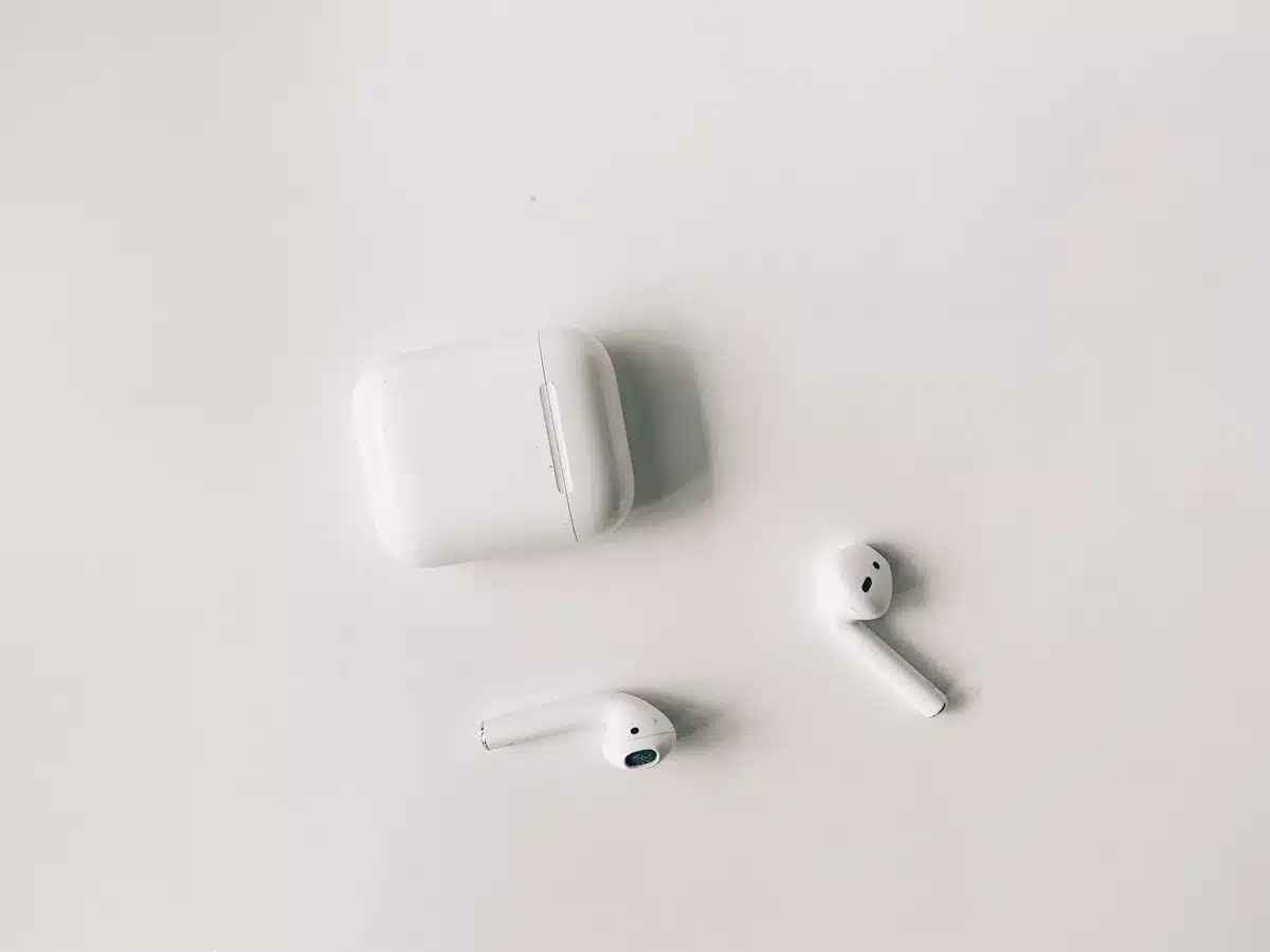 A pair of white earbuds in an open charging case, minimalist studio setting with soft lighting, showing the compact design and sleek finish