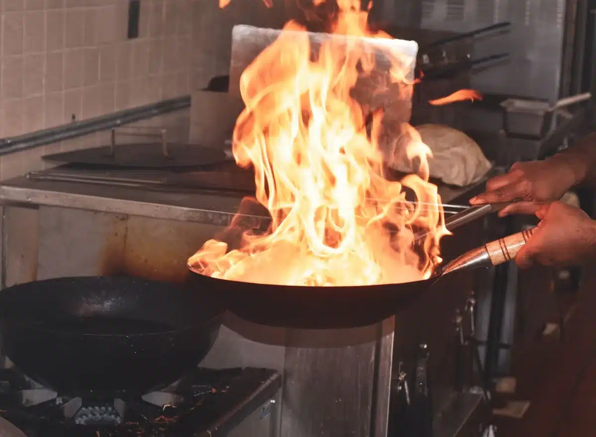 A hot wok or skillet with diced squash pieces sizzling, golden-brown edges visible, steam rising, with a wooden spoon stirring