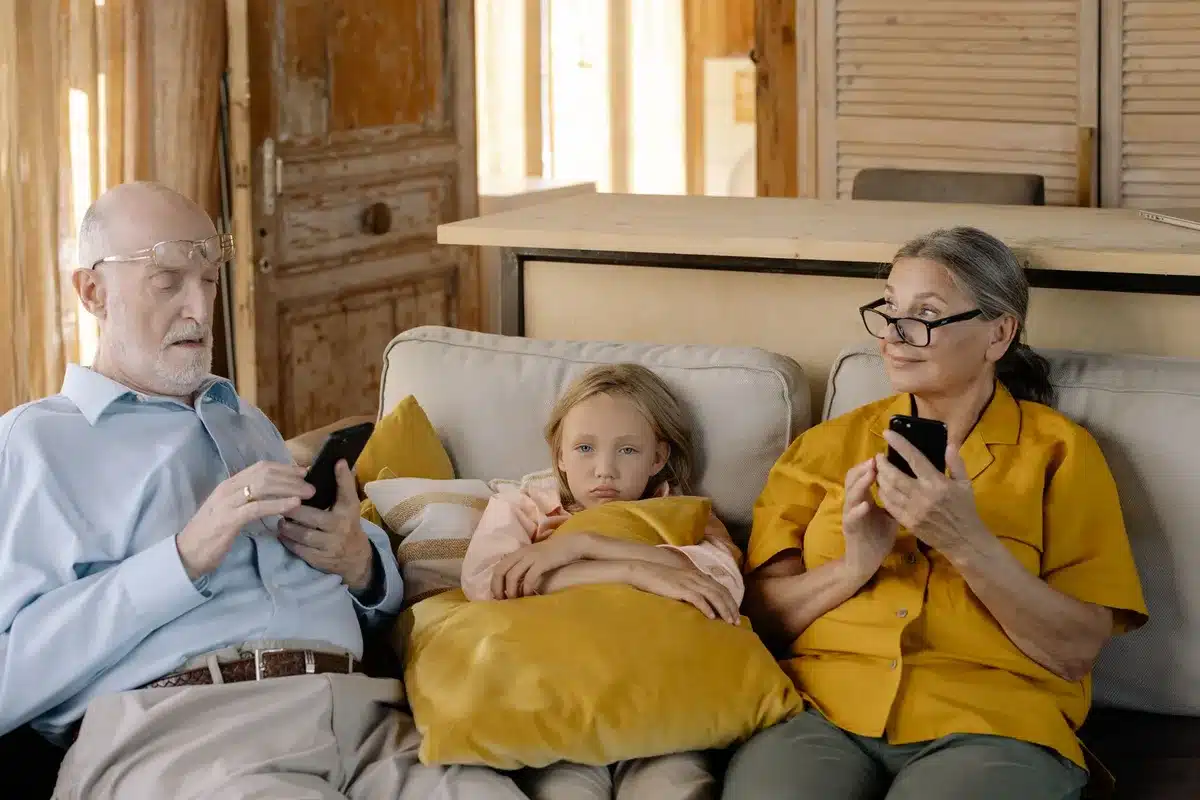 A multigenerational family living room at dusk, with a grandmother, parents, and children visible in soft lighting, looking at a smart speaker display together, demonstrating easy voice control.