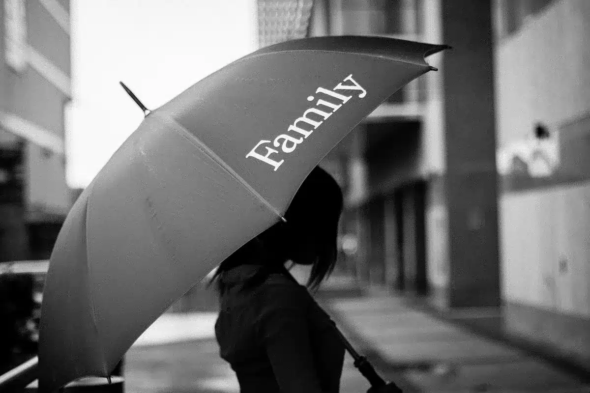 Anonymous silhouette under umbrella beside empty parade route, wet pavement and scattered confetti, cloudy sky
