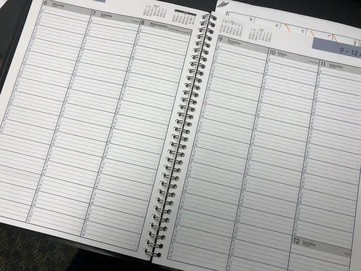 An empty travel planner notebook open on a table next to an unbranded smartphone and a generic boarding pass, a coffee cup at the edge, hinting at last-minute trip prep