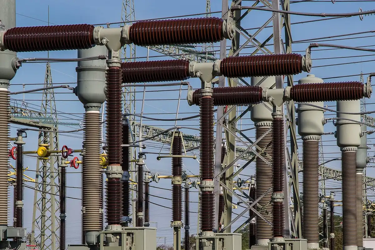 Empty electrical transmission lines and infrastructure in a rural setting, with damaged insulators and disconnected cables visible against a cloudy sky, suggesting infrastructure damage and power outage aftermath.