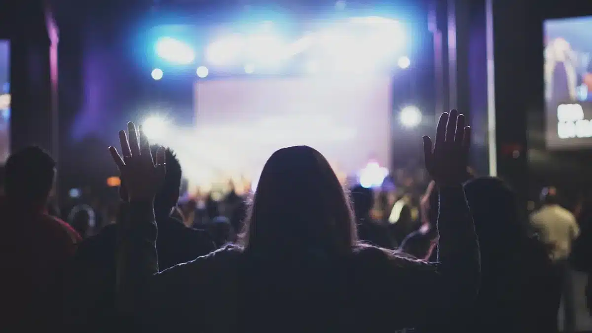 anonymous crowd in dim auditorium looking toward a lit stage with a folded phone silhouette