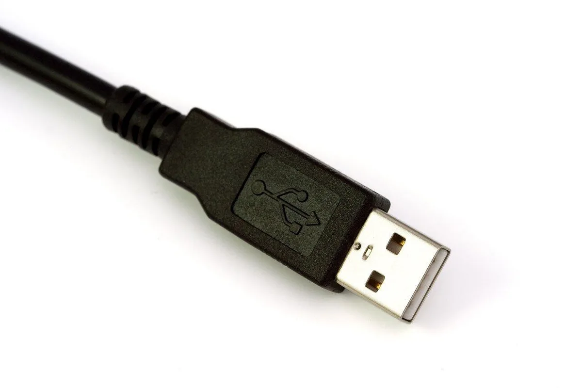 Scene of an anonymous person’s hands holding an unbranded phone above a small wireless earbud case with a cable nearby, suggesting the phone is supplying charge