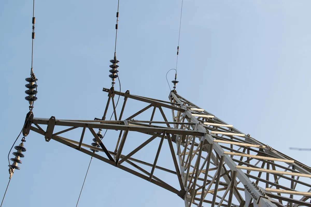Construction site of a new electrical substation with steel framework, transformers, and high-voltage equipment partially assembled against a cloudy sky, showing industrial progress and infrastructure development