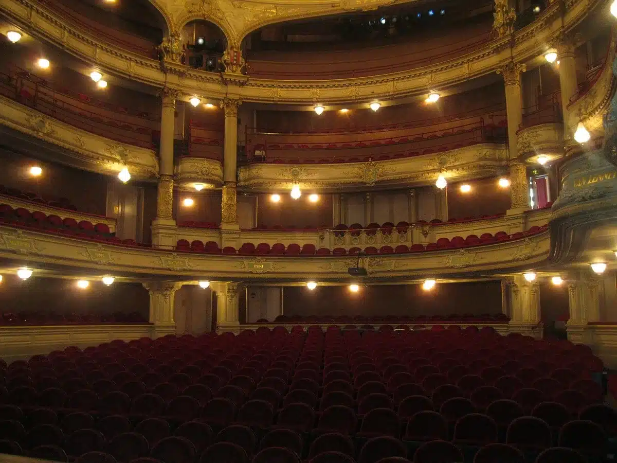 Dark cinema auditorium with empty rows and a glowing large screen, aisle lights on, no people visible