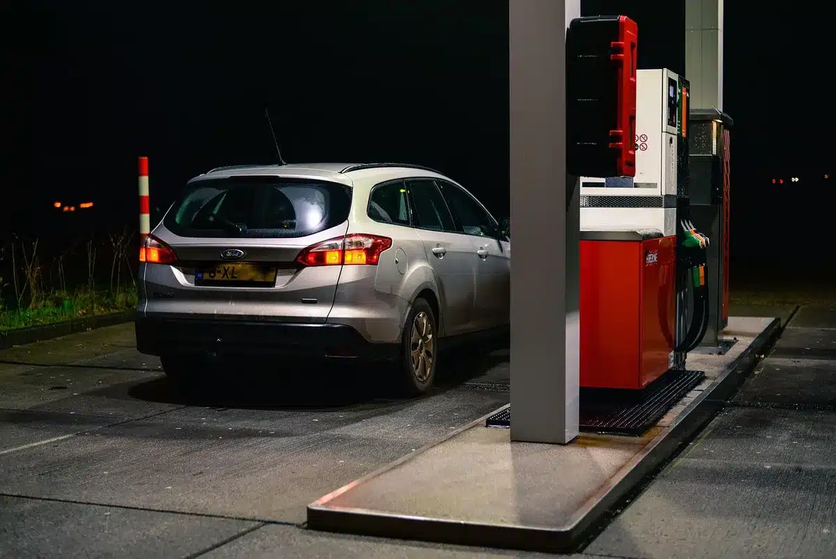 Cartel de precios de gasolina y coches en fila mostrando aumento del combustible