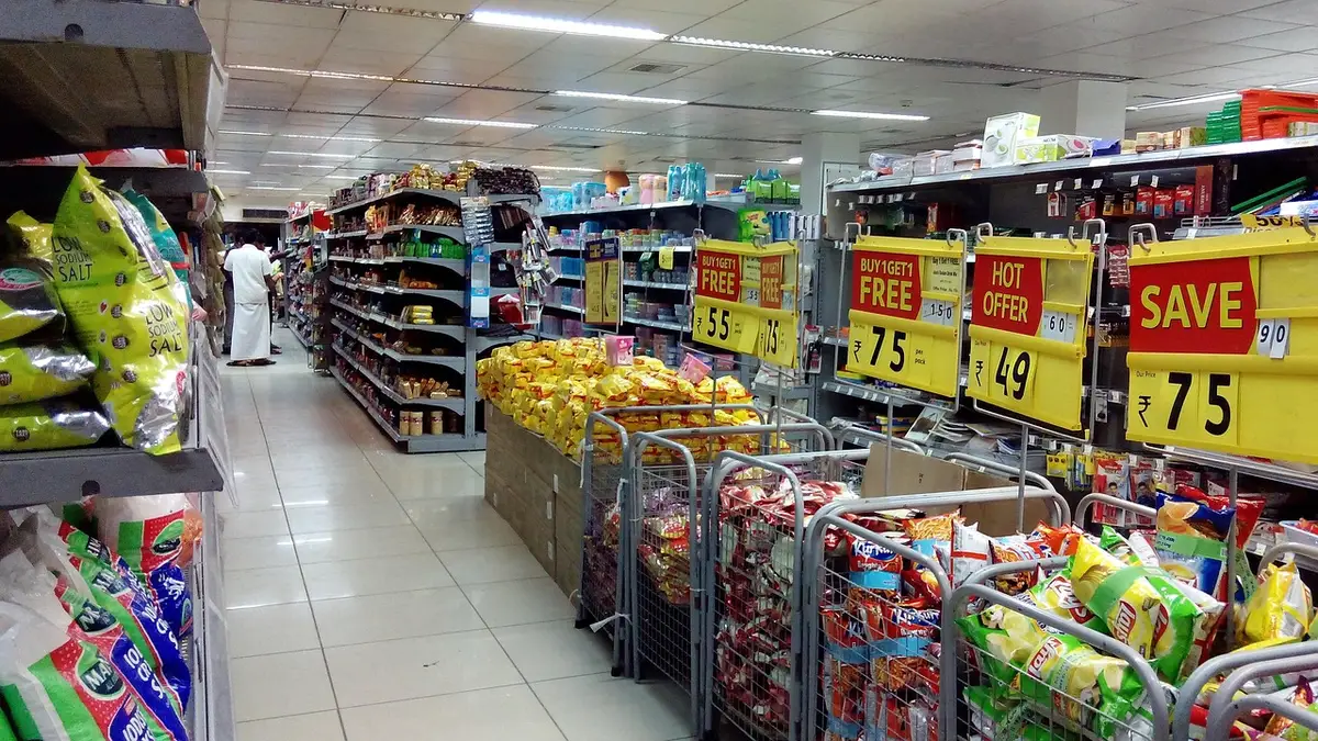 A lineup of physical game cases and digital storefronts side by side, showing price tags with percentage reductions, warm and cool lighting contrasting old versus new retail