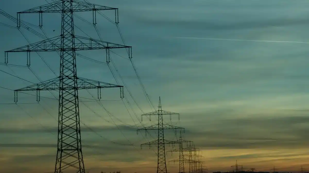 A long distance transmission tower landscape with fiber optic cables stretching across terrain, representing extended signal reach, golden hour lighting, infrastructure perspective.
