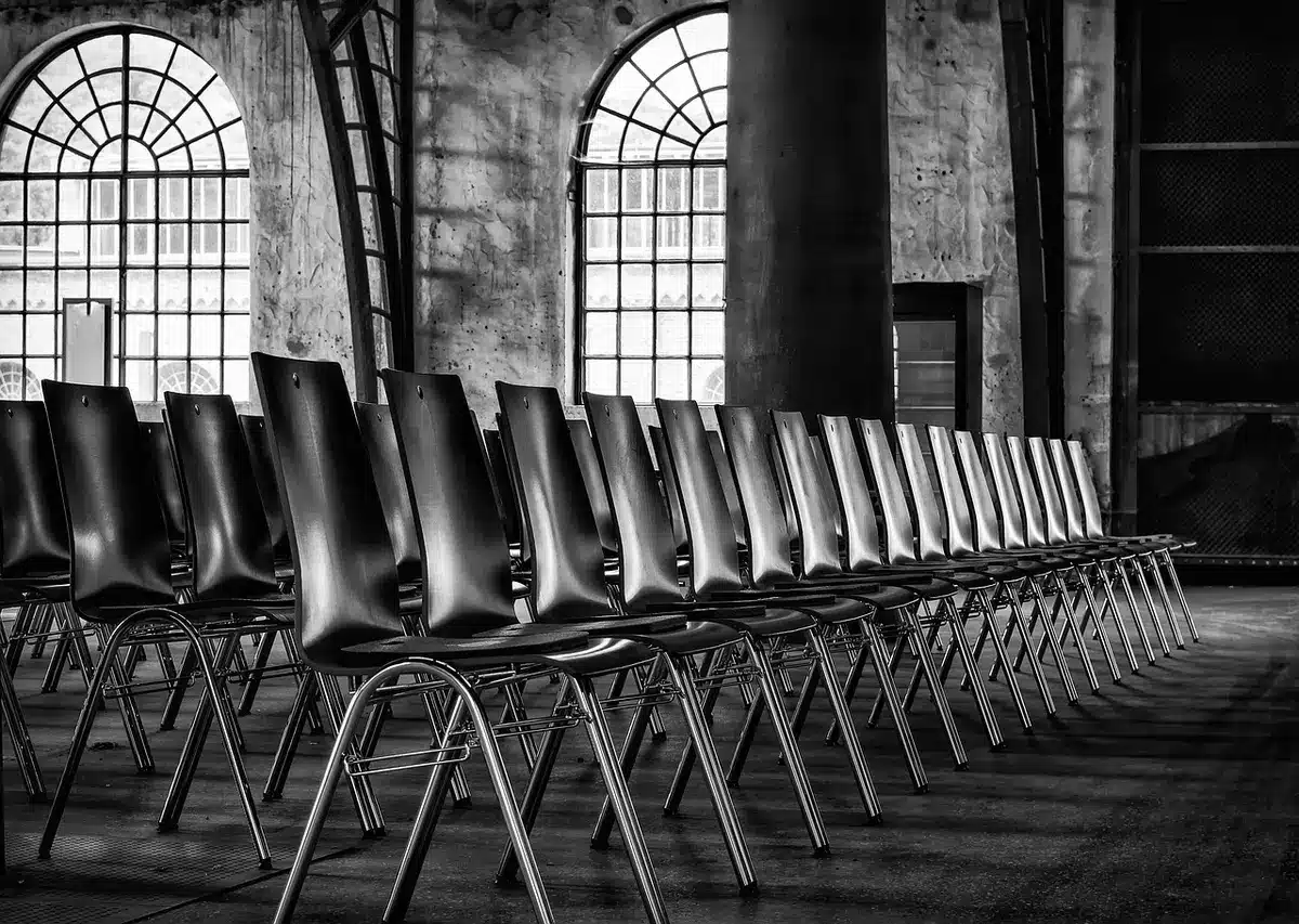 Wide shot of an empty municipal plaza with rows of unbranded folding chairs facing a small stage, soft daylight, no people