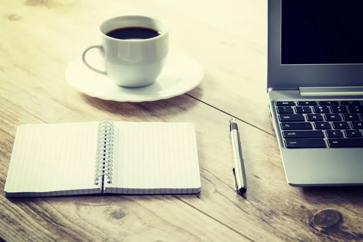 A sleek unbranded laptop closed on a modern wooden desk, an anonymous smartphone face-down beside it, soft daylight through a nearby window, curiosity-inviting scene