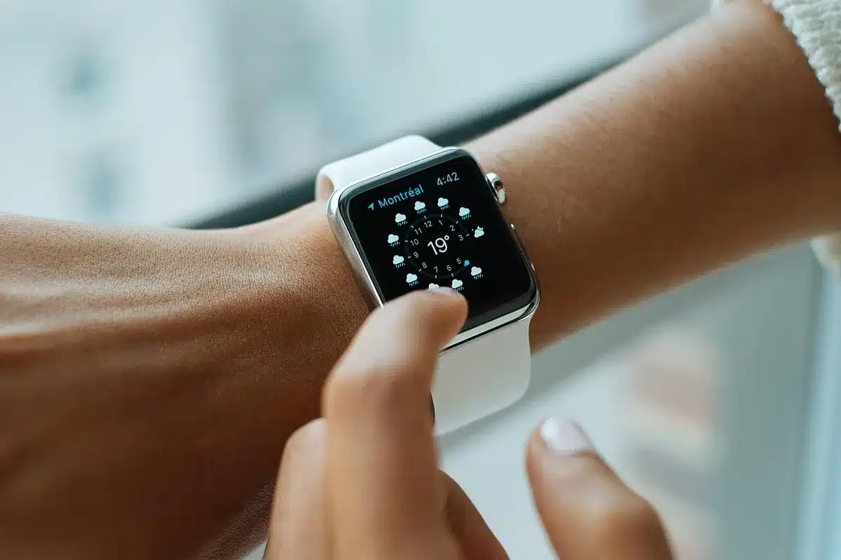 An anonymous hand wearing a smartwatch with AMOLED display, showing health metrics and heart rate data on screen under bright outdoor light, with soft focus blurred background.