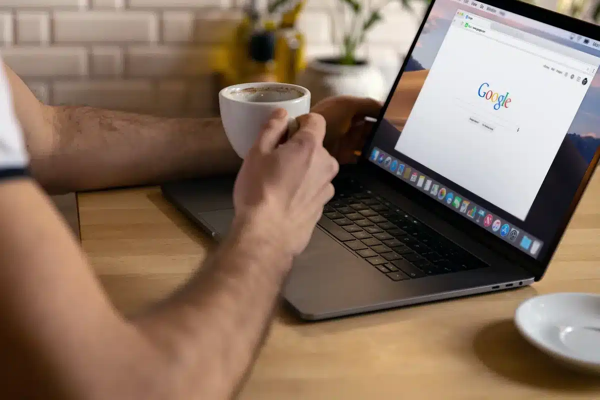 An anonymous close-up of hands typing on a laptop with an open browser showing a generic product card, out-of-focus coffee cup in background
