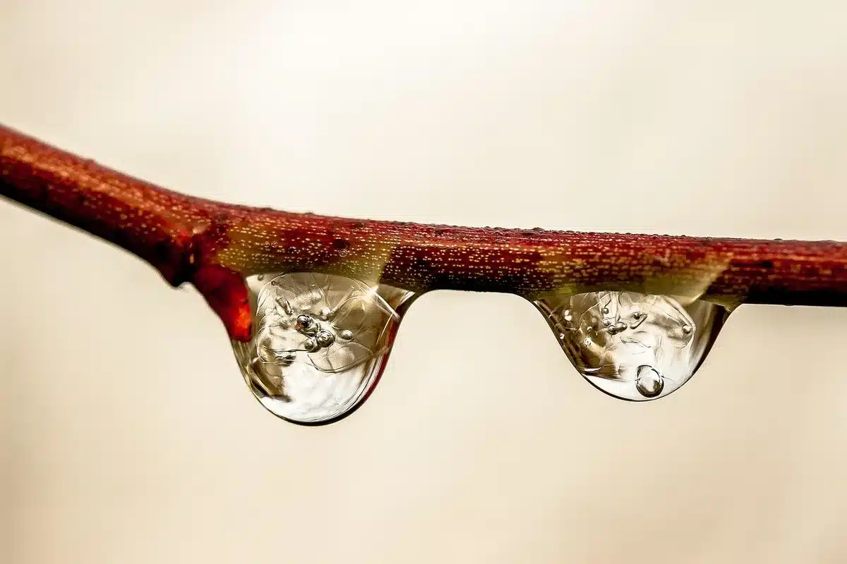 Water droplets sliding across a hydrophobic surface, acquiring electrical charge, with a metallic surface visible beneath a protective coating