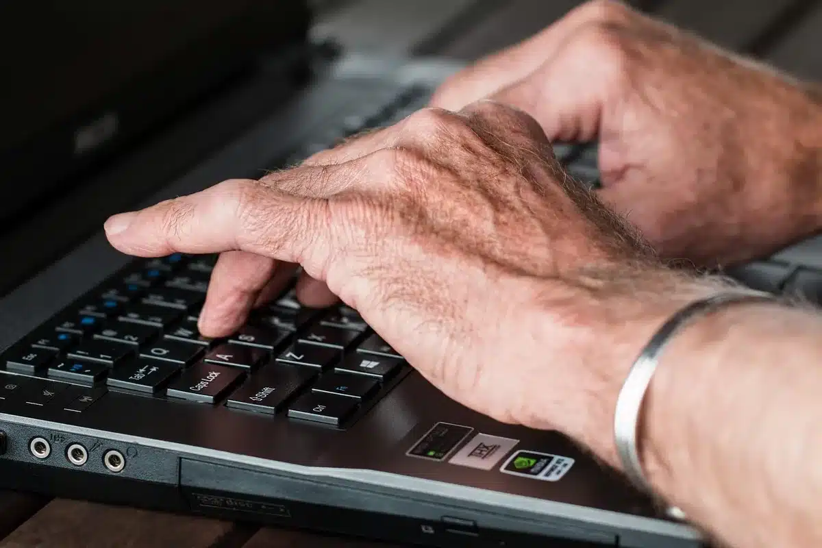Close-up of anonymous hands typing on an unbranded laptop, a notepad with handwritten notes beside it, blurred office environment in background
