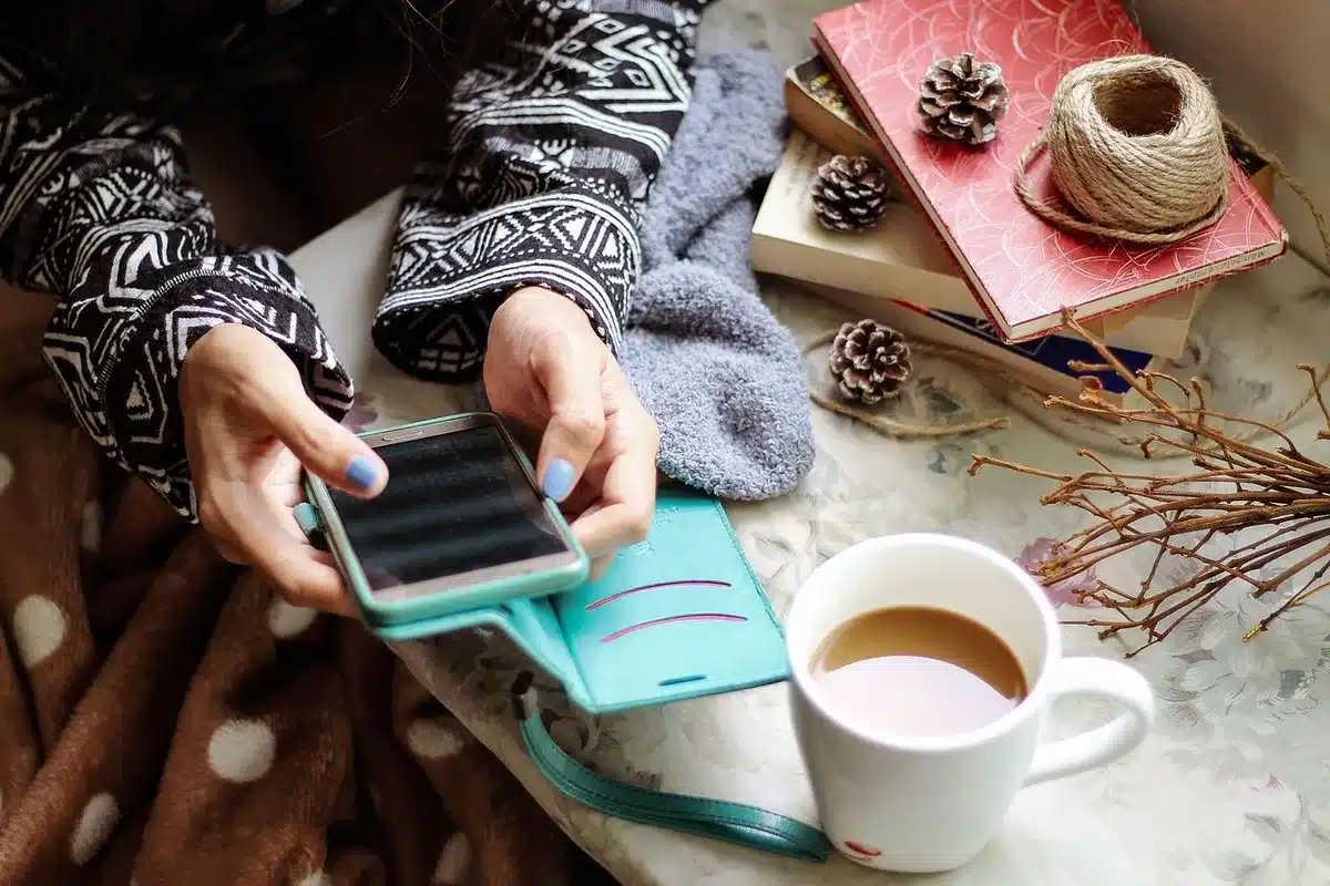 A small unbranded countertop scene showing a merchant's hand holding a generic smartphone upright ready to receive a tap payment; no logos or faces visible