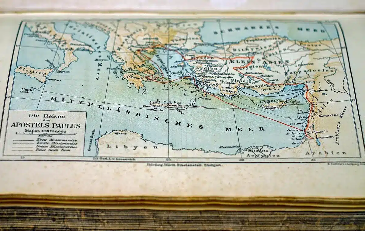 Empty regional administrative office with a stacked set of unlabelled maps and boundary documents on a wooden table; distant anonymous hands pointing at a map
