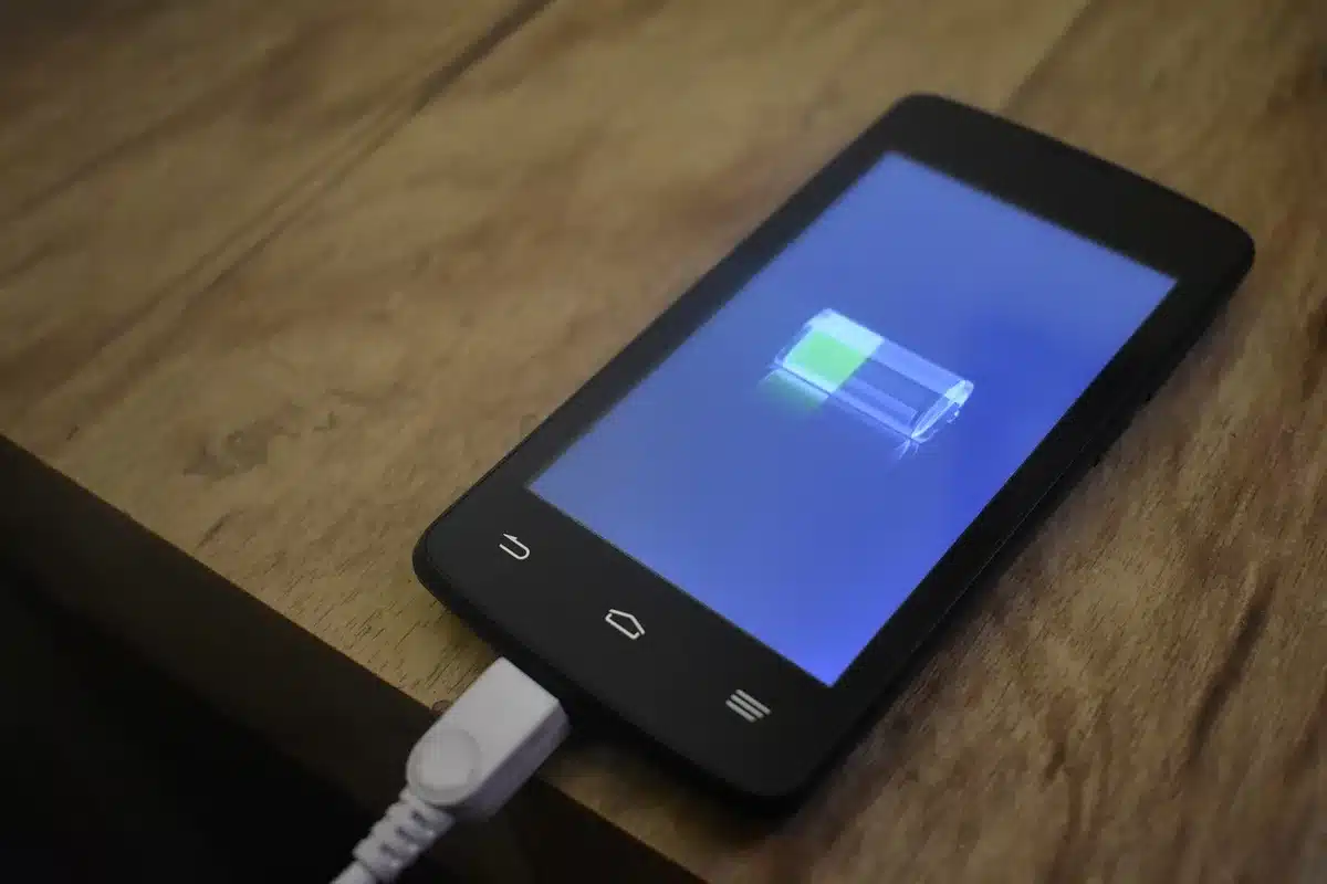 A close-up of a phone's battery indicator showing full capacity, with a charging cable coiled nearby on a neutral background, warm lighting highlighting the battery percentage.