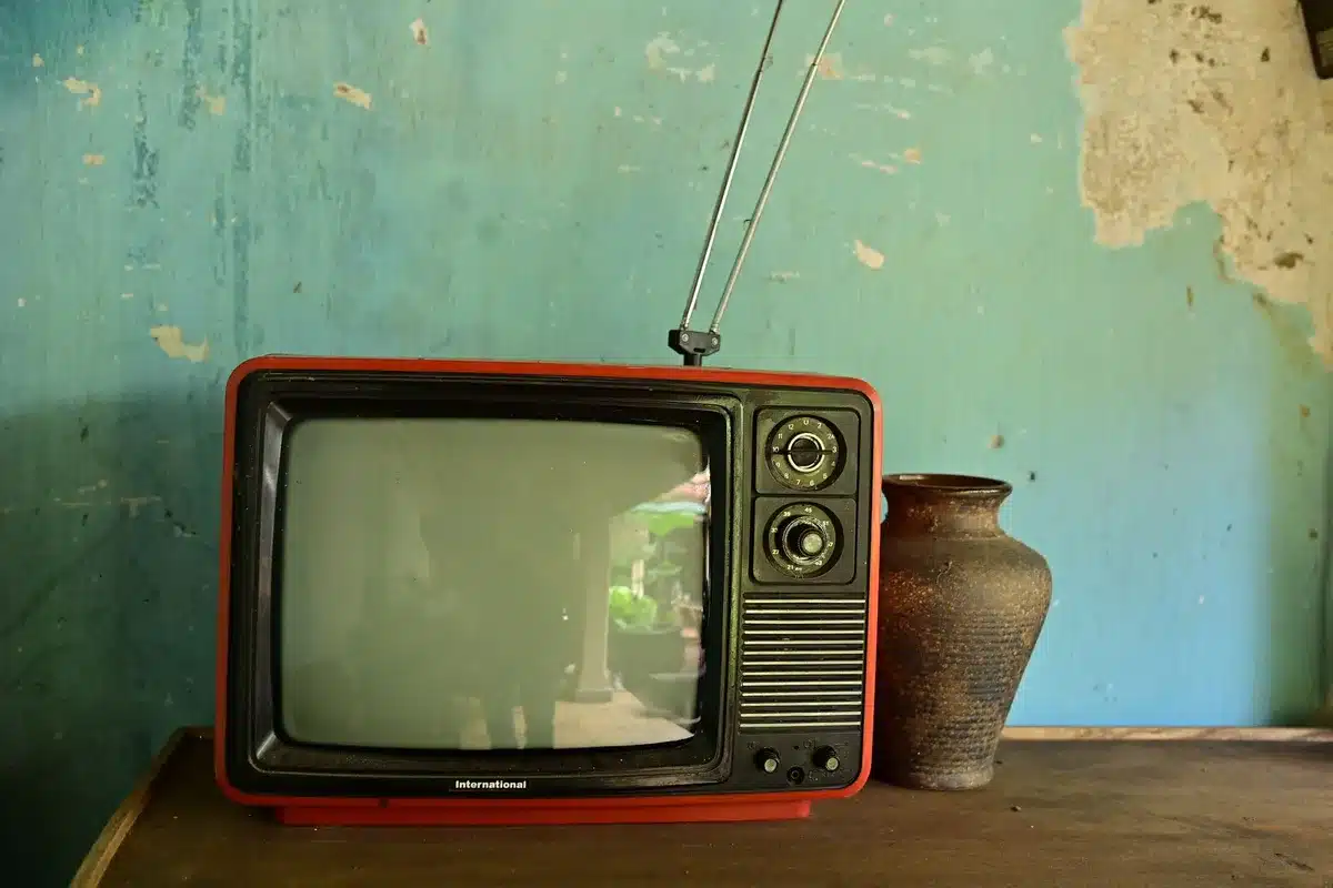 An empty modern living room with a large unbranded TV screen glowing warmly, no people, a low coffee table and a remote on it, soft reflections on the screen