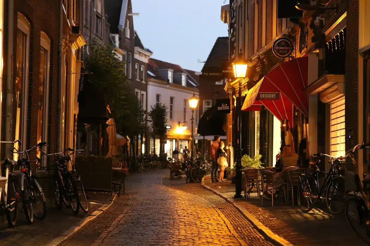 Narrow colonial-style street at night with anonymous silhouette walking away, warm lamplight and closed doors