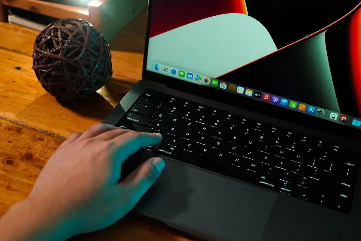 Close-up of a laptop keyboard with RGB lighting and an anonymous hand hovering, shallow depth of field