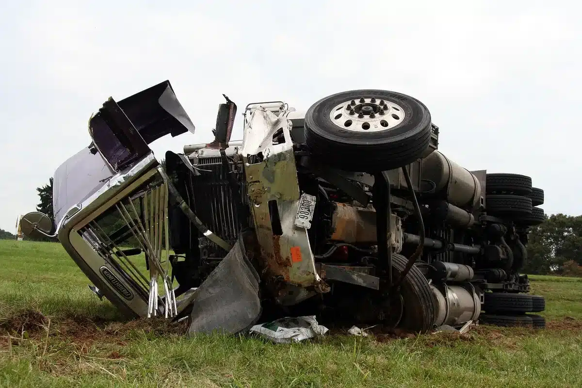 A toppled unbranded transport truck on a two-lane highway at night, tyres up, emergency cones and anonymous figures working at scene