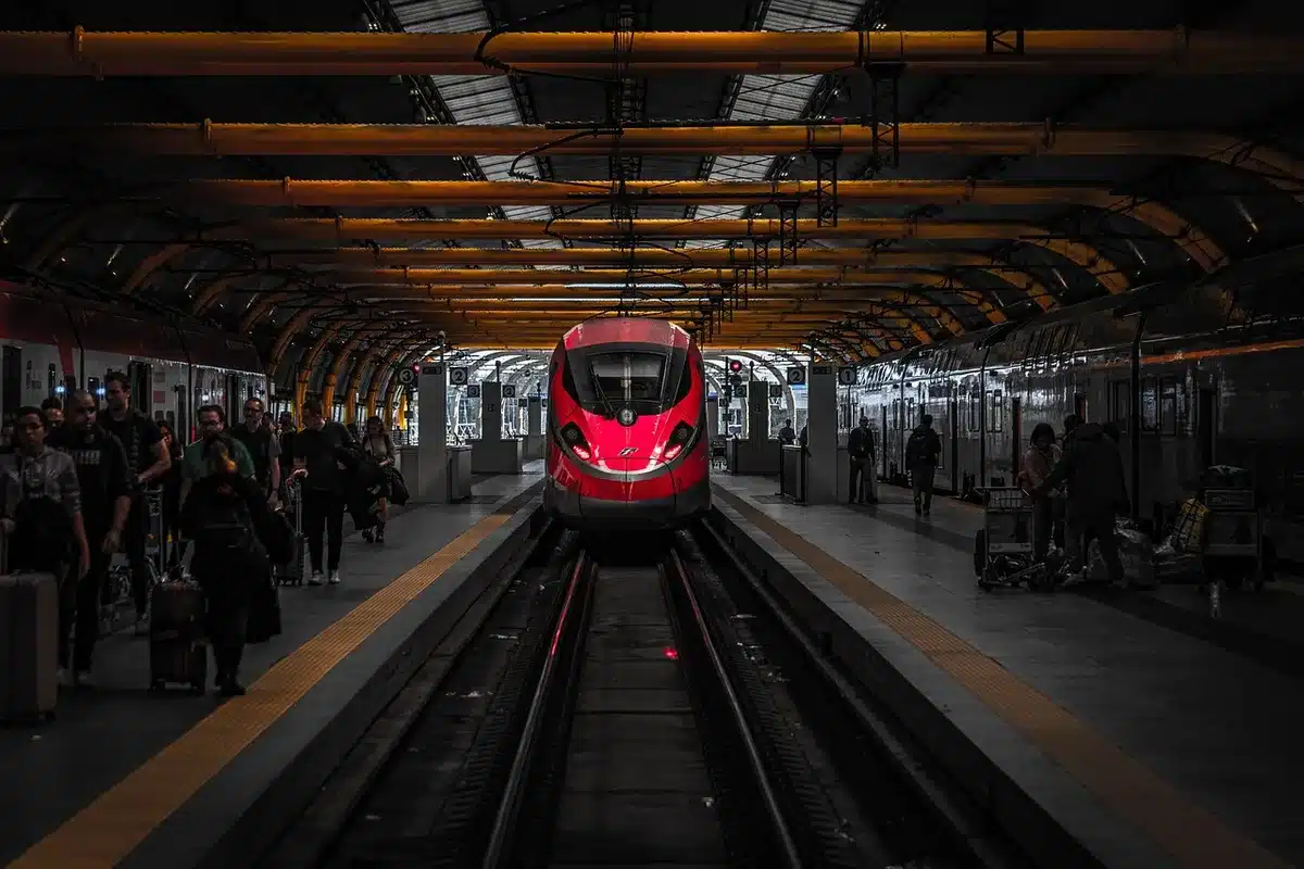 Empty train station platform with luggage on trolleys and distant anonymous passengers moving toward a mezzanine