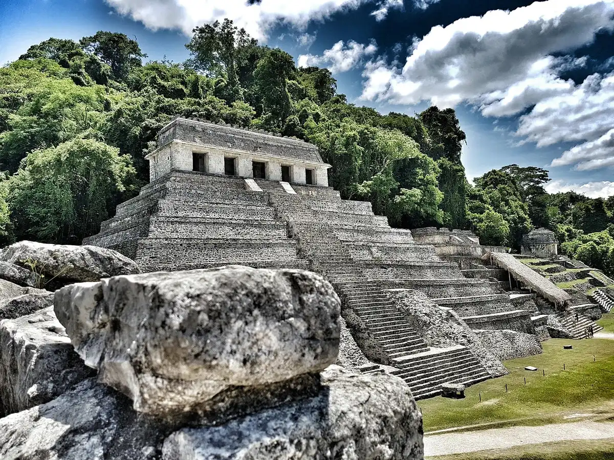 Path through a low-ceilinged Maya site with stone structures and shaded trail, no people, tranquil archaeological setting