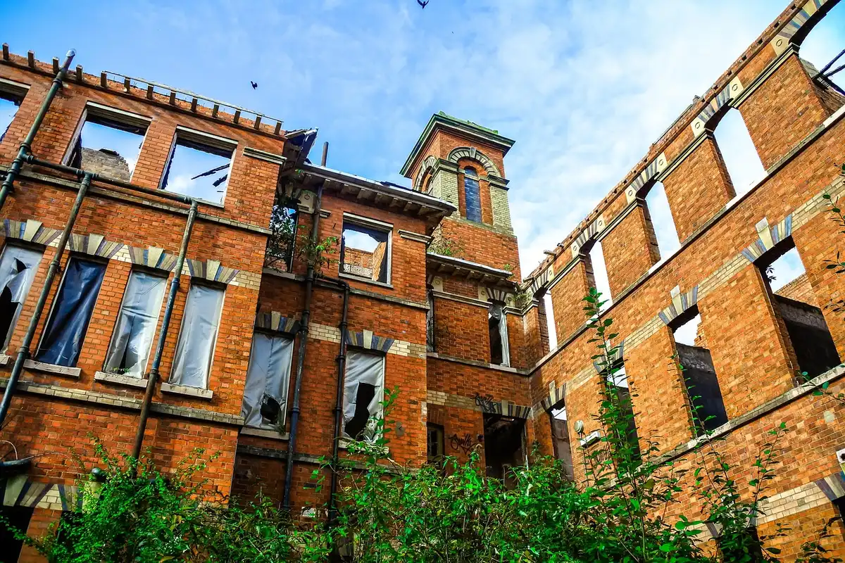 Broken colonial facade with loose bricks and a taped-off sidewalk, no people visible, wet pavement after rain