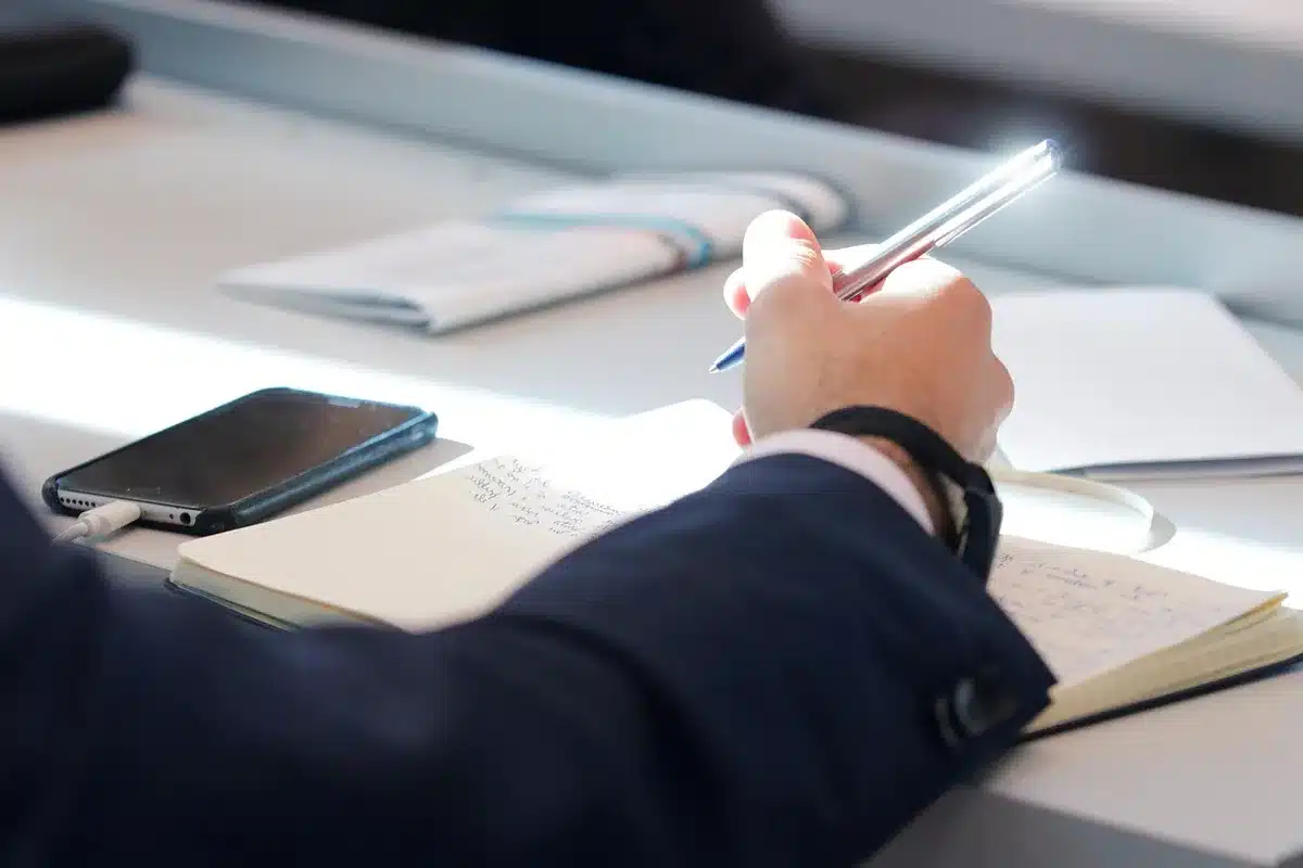 A dimly lit desk scattered with handwritten notebooks, old audio cassettes and loose judicial documents, a fountain pen resting on an open page