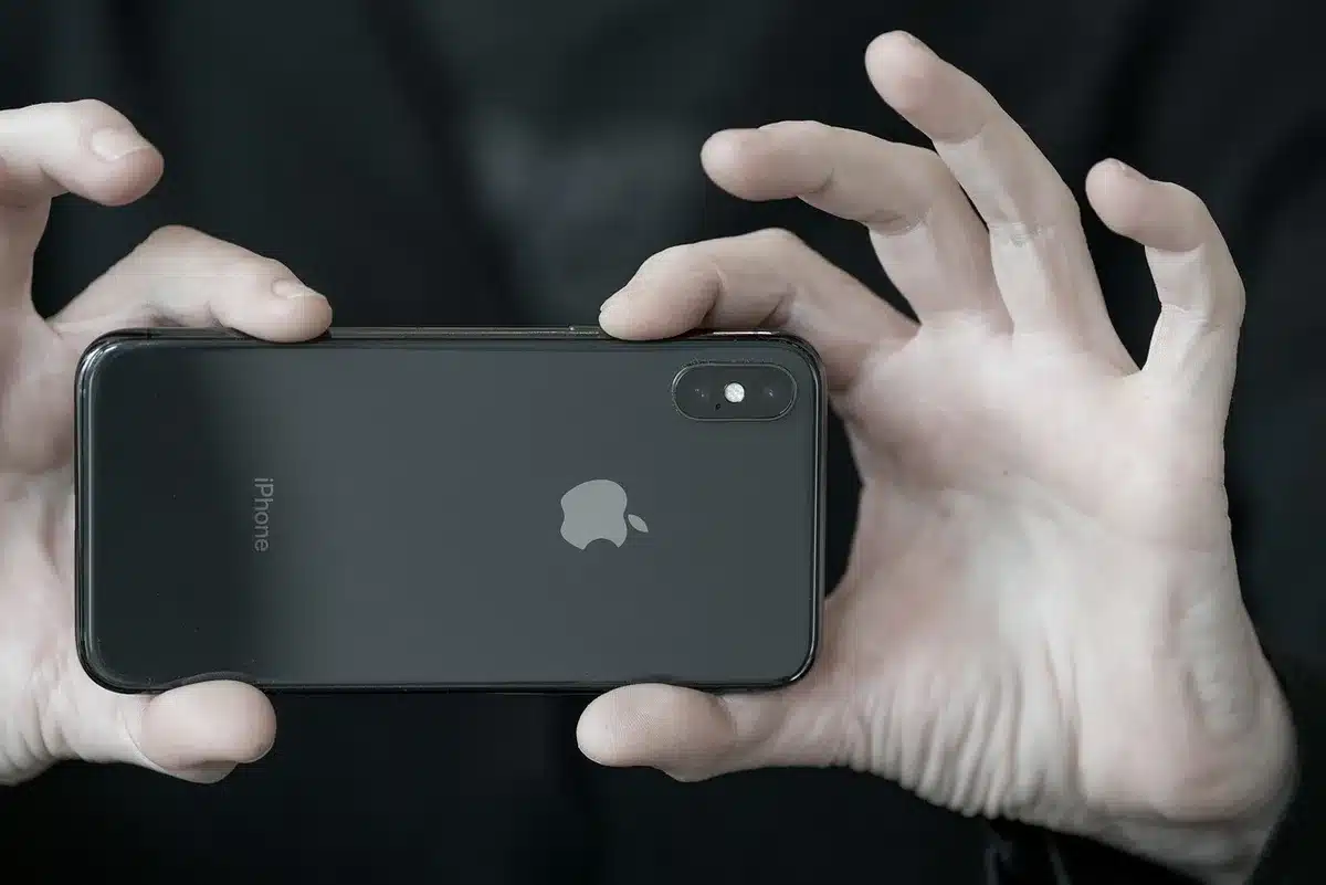 An anonymous hand holding an unbranded smartphone over a neutral background, back visible with textured finish, no brand or logo