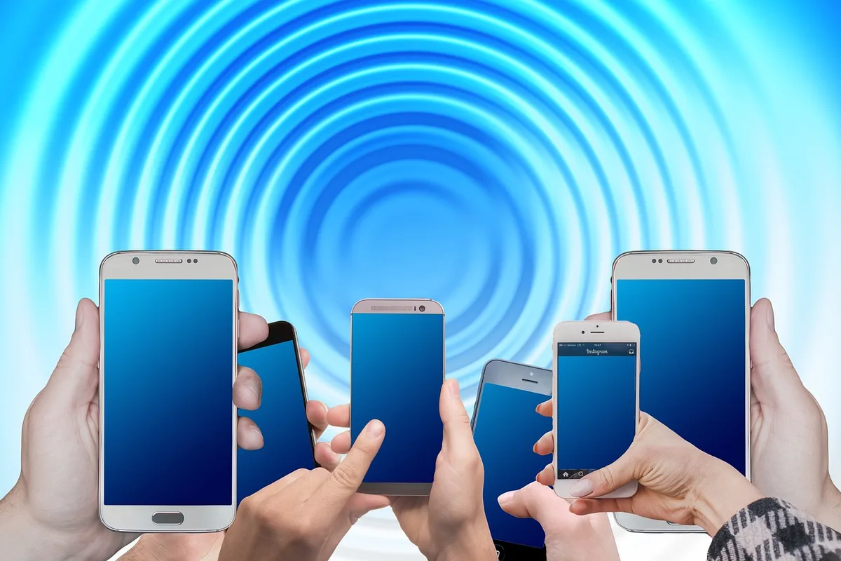 Anonymous hands holding an unbranded smartphone showing signal bars and a blurred urban skyline through a window, implying mobile connectivity and device dependence
