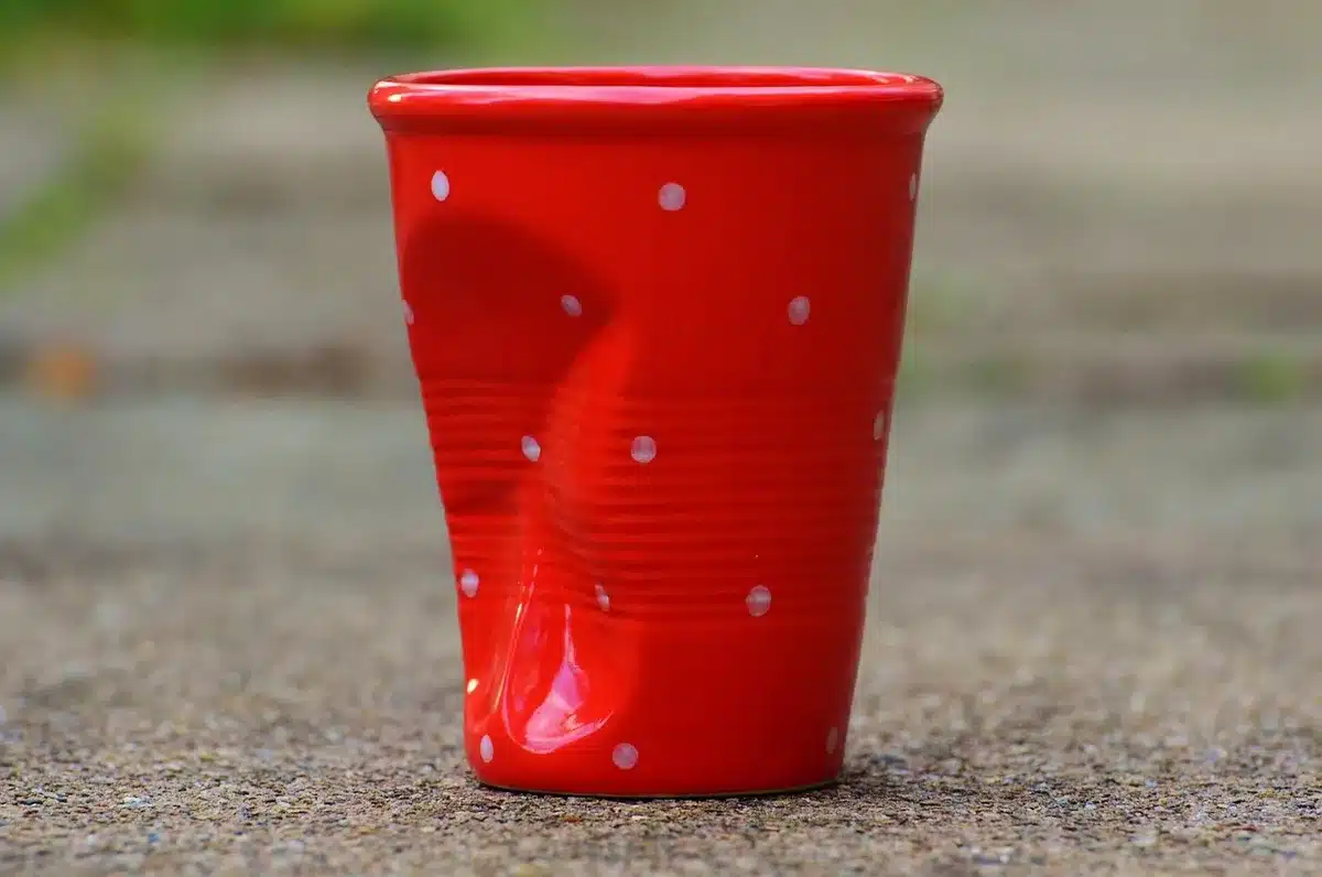 an overturned ceramic mug on a wooden table with its unglazed ring visible, a sharp unbranded kitchen knife blade held at a low angle above it