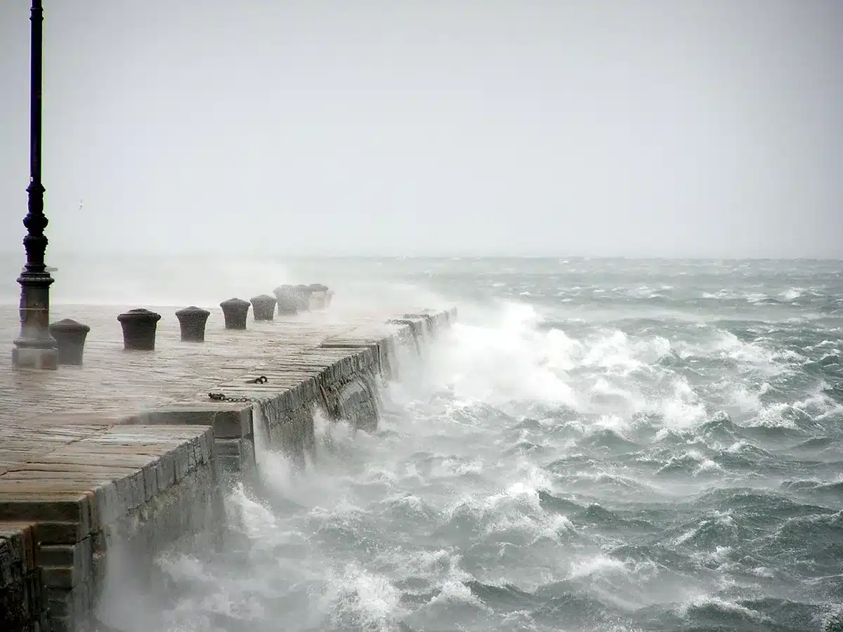 Empty wooden pier battered by storm surge and scattered debris, distant dark clouds over the bay