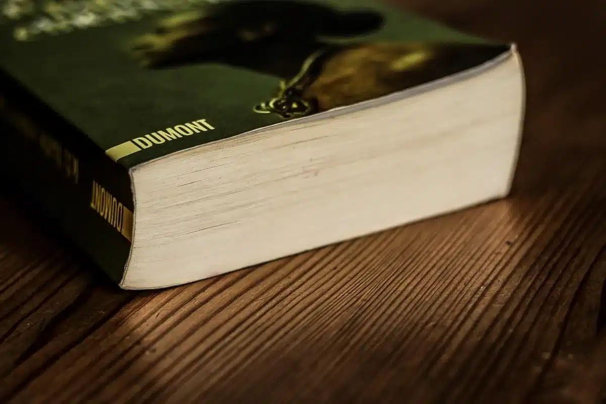 A close-up of an unbranded paperback book on a wooden table, next to a pair of reading glasses and a blank notebook, evoking study and reflection