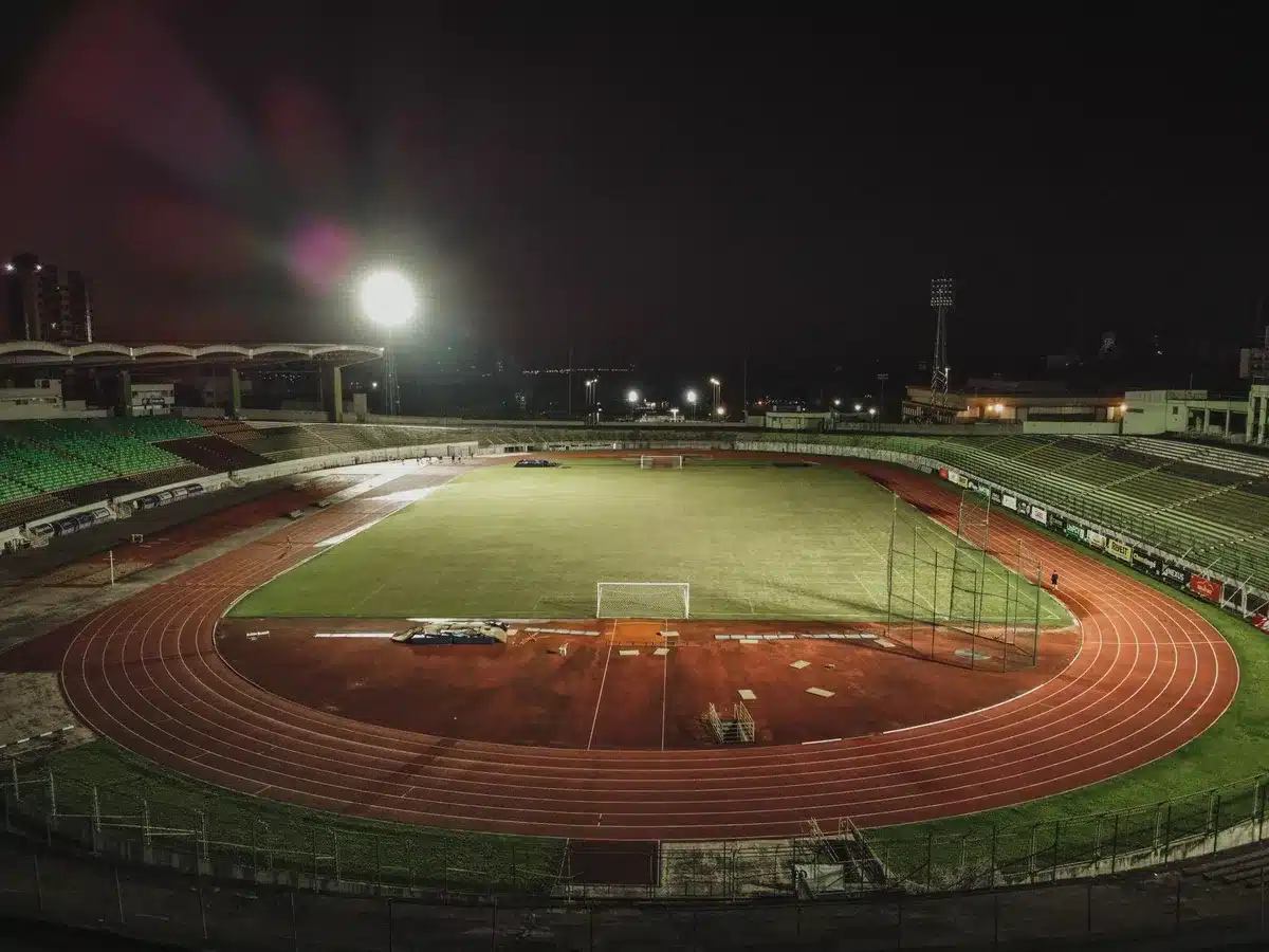 Empty small stadium at dusk with an anonymous goalpost and worn pitch, hinting at a local match about to start