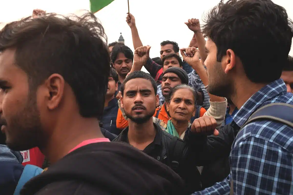 Anonymous crowd outside a municipal building holding plain banners, faces blurred, overcast sky