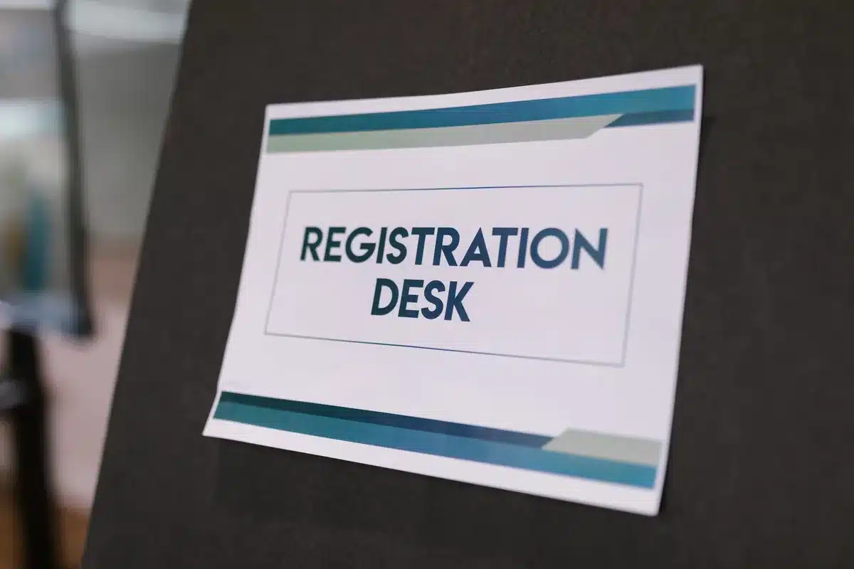 Anonymous hands of an adult filling out a generic registration form at a kitchen table with a smartphone nearby showing a social media feed