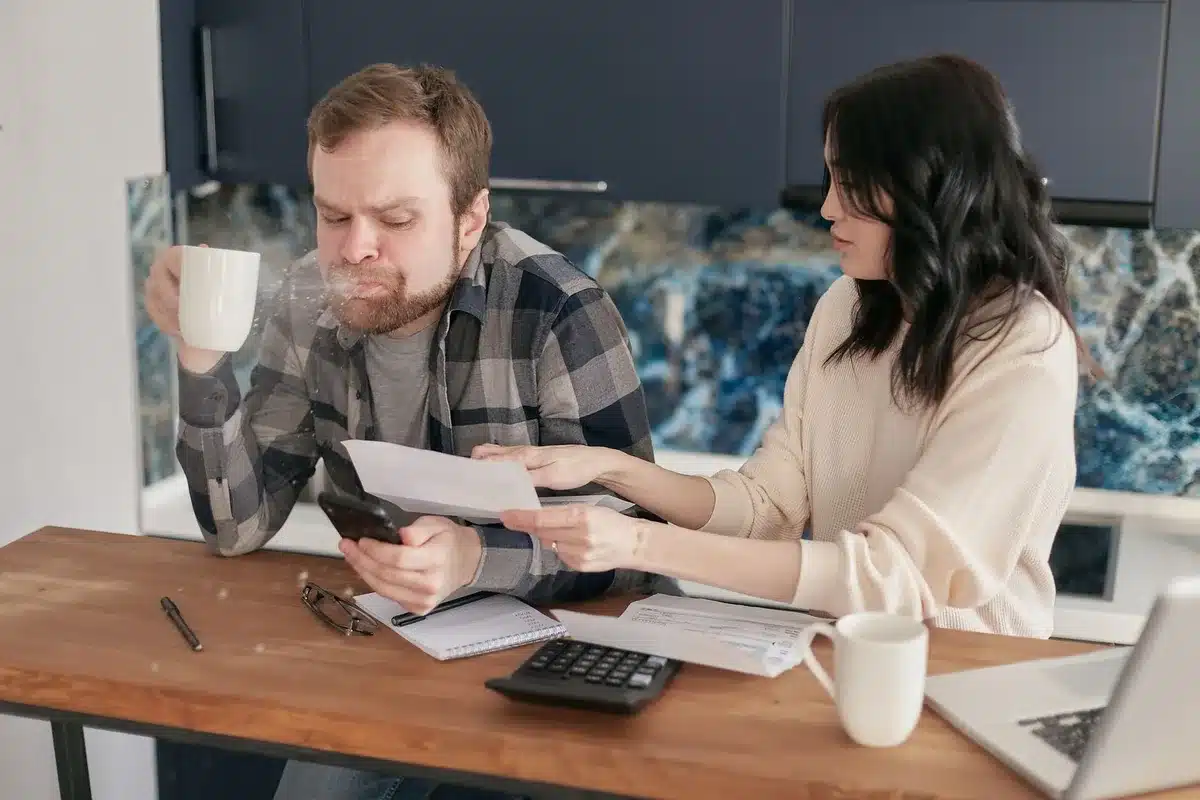 An empty office desk with a closed laptop, a printed generic invoice on top, and a smartphone showing an email inbox in soft focus