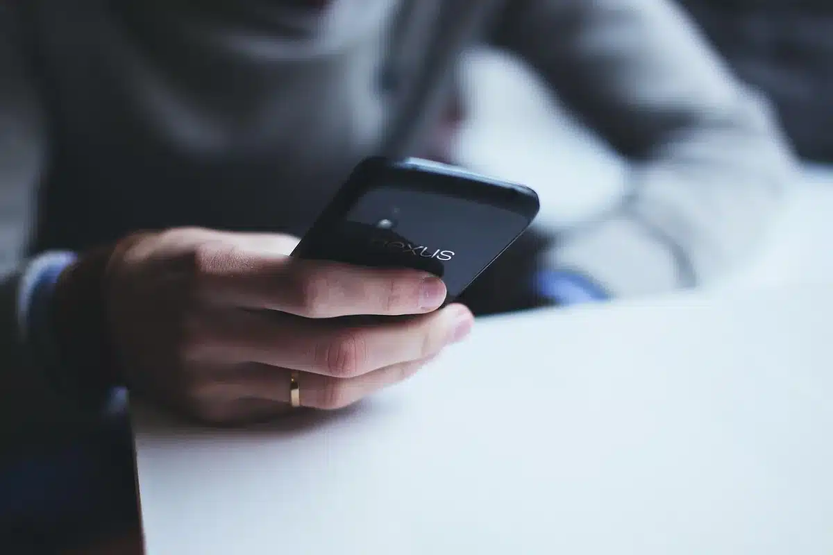 A blurred anonymous person on a phone, viewed from behind, a computer screen showing an inbox in the distance