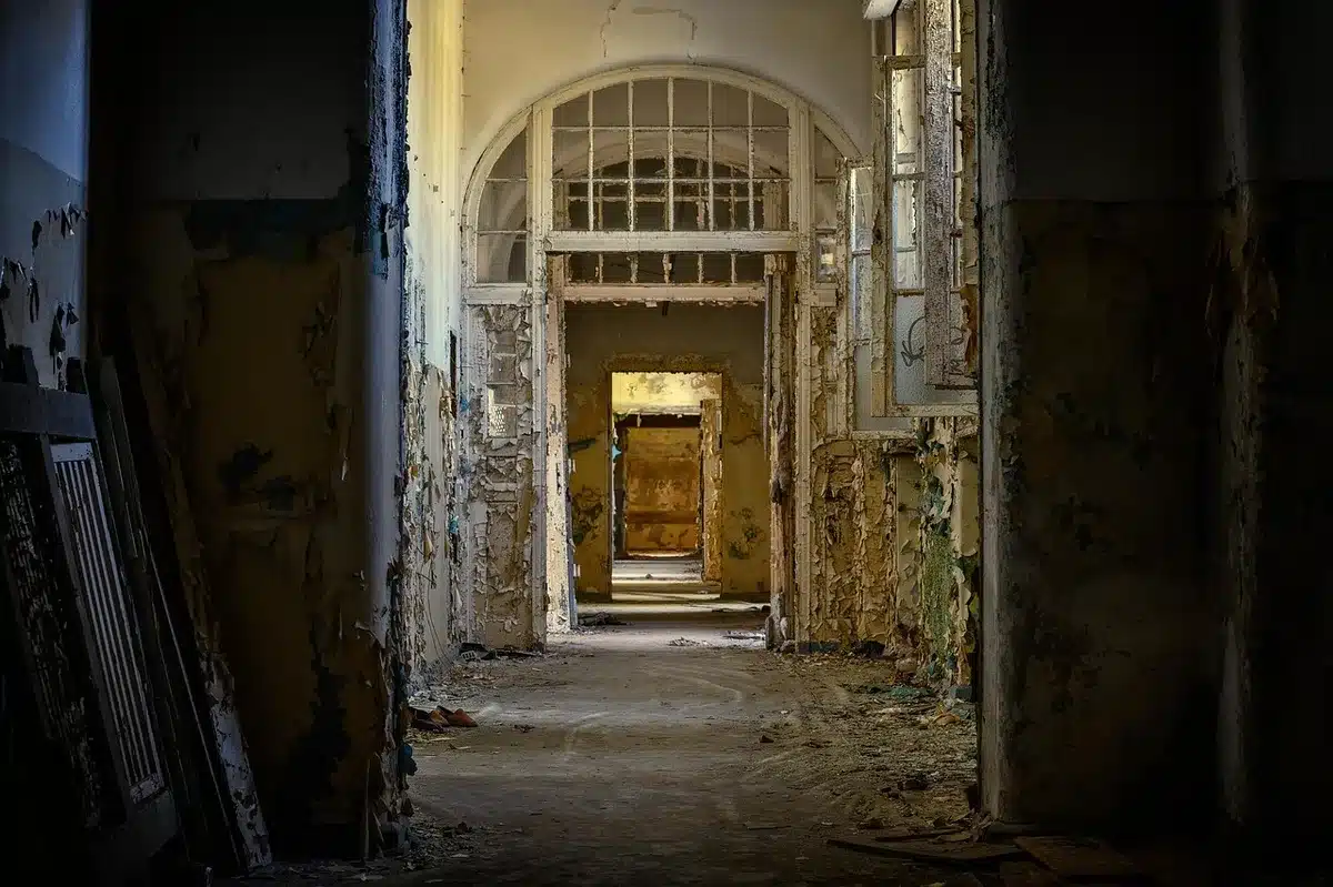 Empty school hallway with lockers and rain-darkened windows, no people visible, a mop bucket at the end of the corridor suggesting readiness