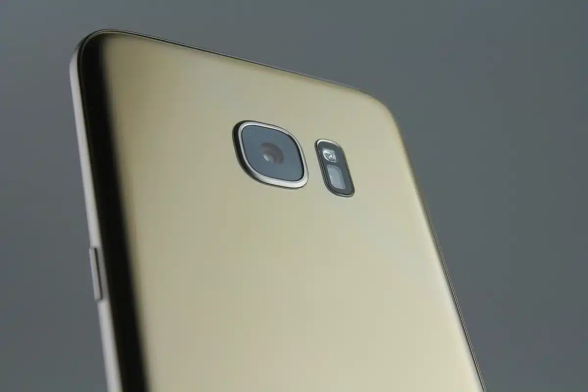 An anonymous pair of hands holding an unbranded phone from the back, showing a triple camera bump and a blurred retail box in the background