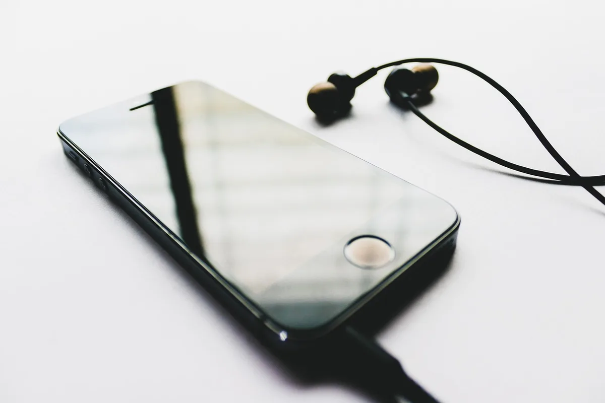 A close-up of an anonymous smartwatch resting on a gym towel with a pair of Bluetooth earbuds beside it, downloaded music visible as generic waveform icons on the screen