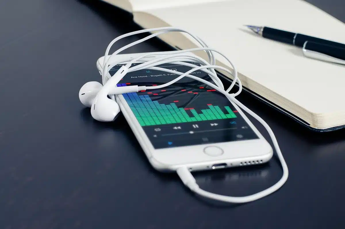 An anonymous pair of Bluetooth sport earbuds lying next to a generic outdoor watch on a wooden bench, hinting at a phone-free run with downloaded playlists visible as icons