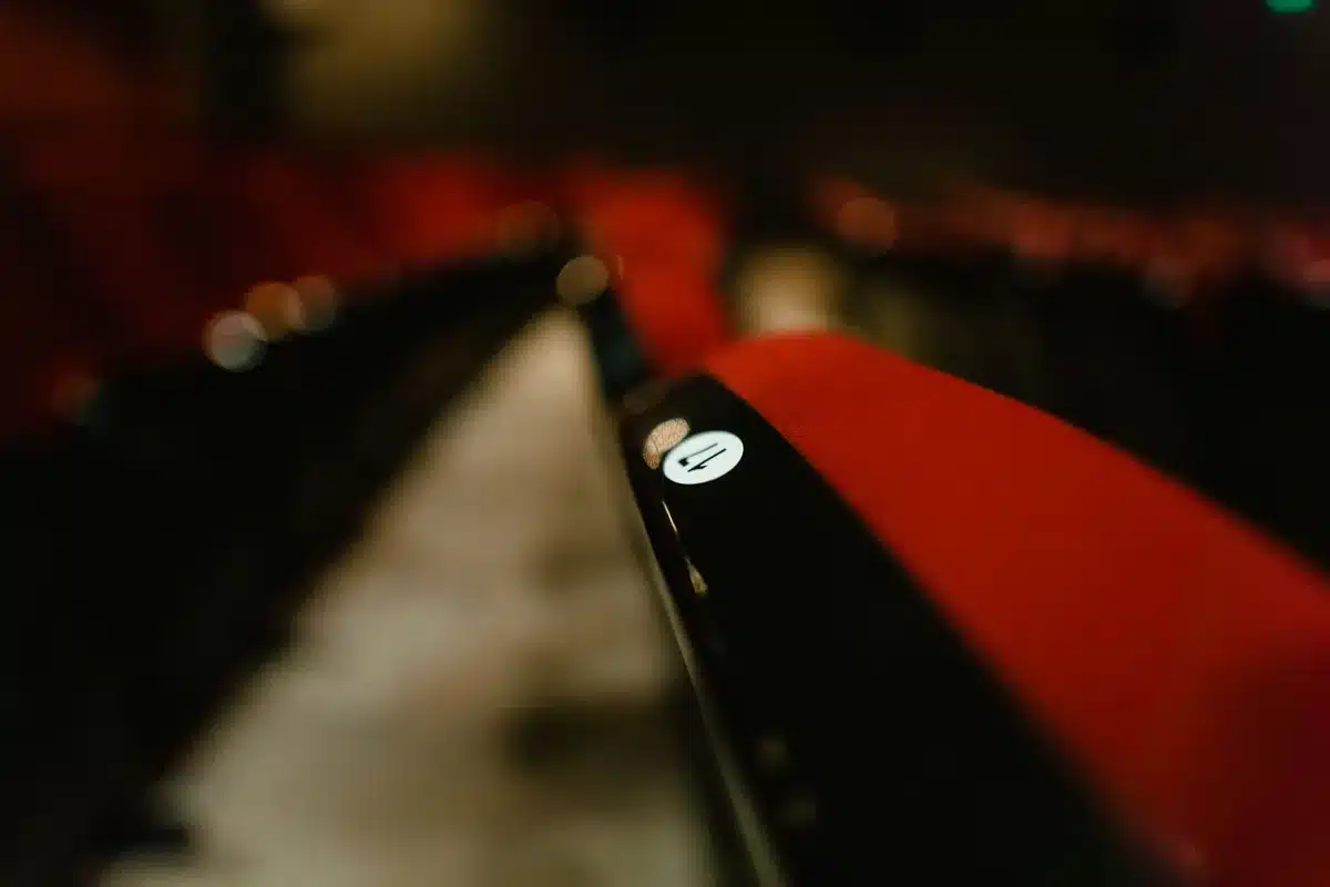 Empty theater seat facing a dark screen with a single spotlight, a paperback mystery novel on the seat, no people