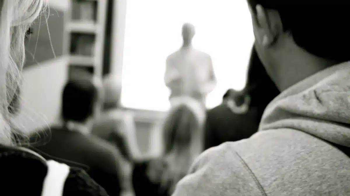 Anonymous crowd of students in auditorium, some heads turned, a few hands raised; faces blurred or turned away, no logos