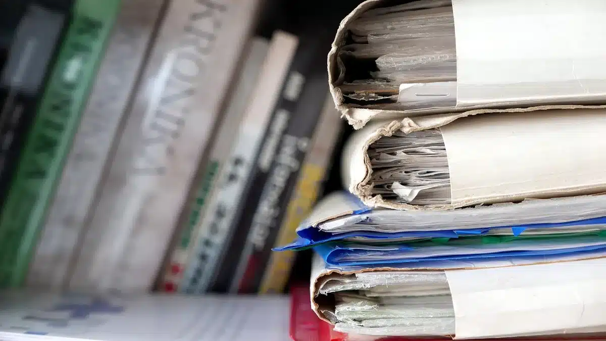 Anonymous close-up of hands filling an unbranded invoice form next to a generic stamp and a ledger book, no logos visible
