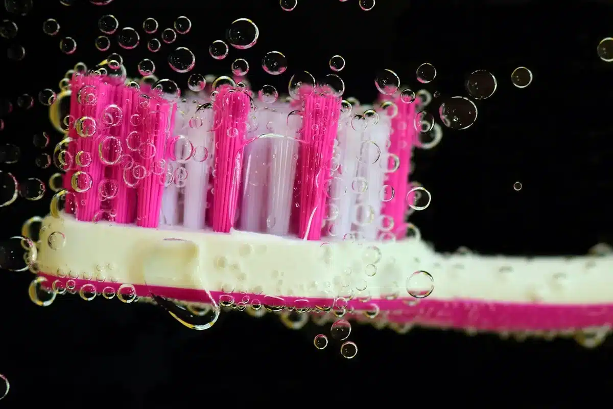 A close-up of an unbranded electric toothbrush with an anonymous hand holding it over a neutral bathroom counter, camera lens visible but non-identifiable
