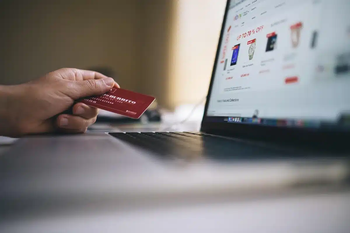 Close-up of anonymous hands holding a credit card and a smartphone showing a shopping cart page, screen glare, no logos visible