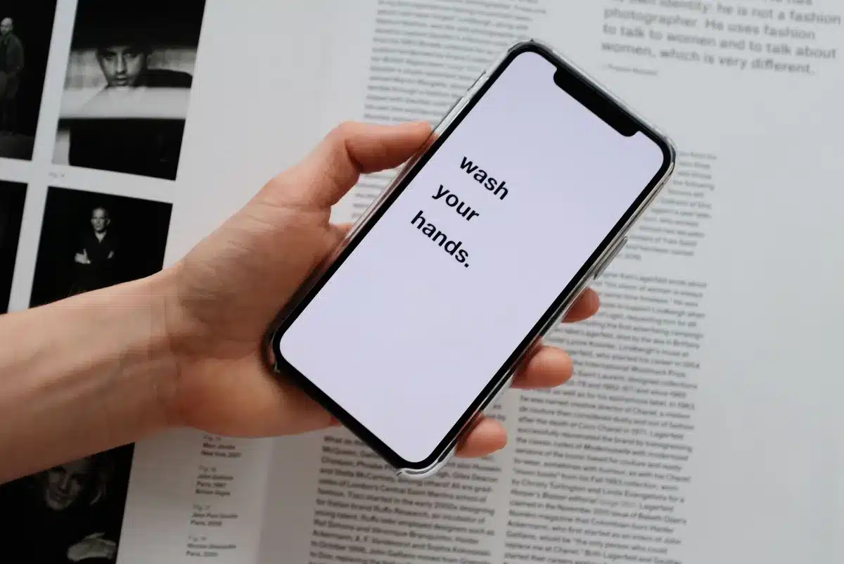 Close-up of anonymous hands tapping a smartphone screen on a wooden desk, blurred packaging box in background, no brand visible